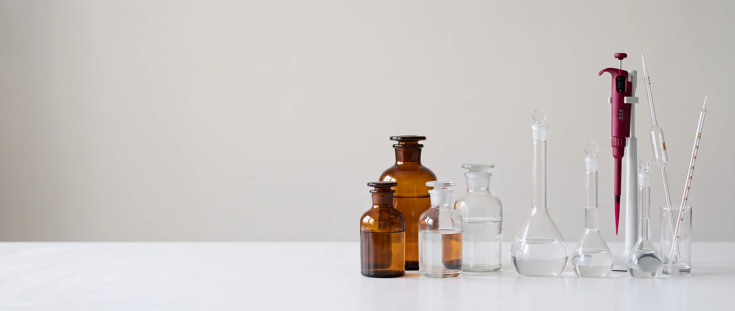 Amber reagent bottles, volumetric flasks and a pipette on a white lab bench